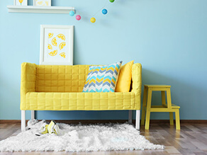 Bright_Kids_Room_Blue_Wall_timber_floorboards_yellow_plush_couch_stool_fluffy_white_rug_artwork
